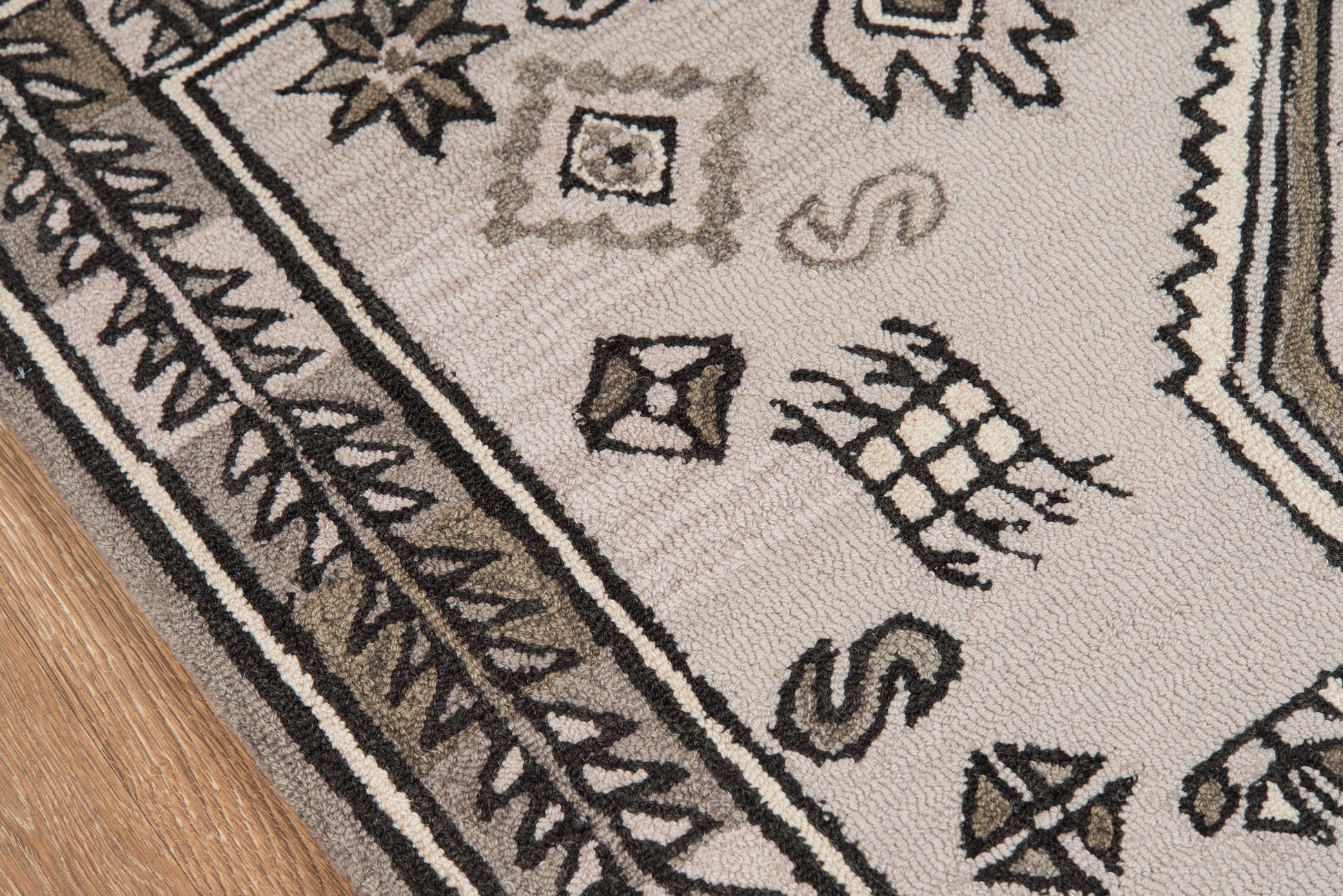 Beige-gray oriental-inspired area rug with black geometric motifs and decorative border on wood floor.