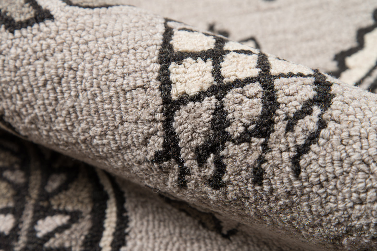 Gray geometric patterned rug close-up with cream accents and black lines; thick plush pile.
