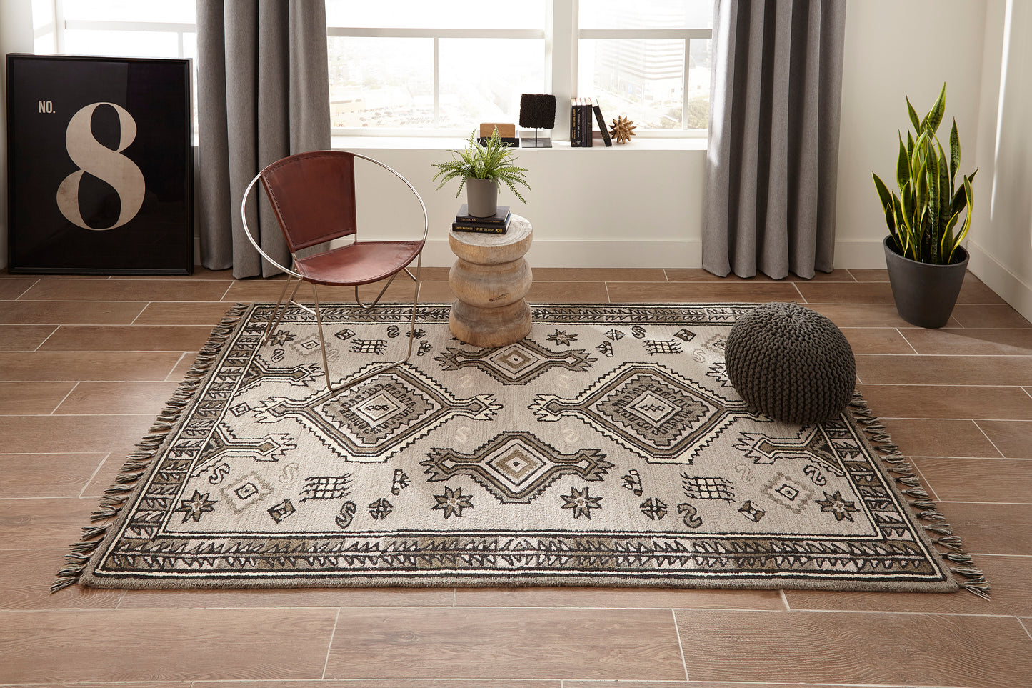 Geometric gray-beige rug with fringe on wood floor; boho living room with leather chair, pouf, plant, and No. 8 art.