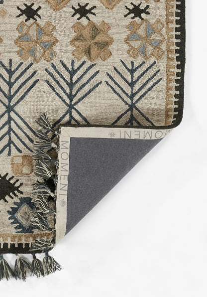 Beige woven rug with navy branch motifs and tan geometric flowers, dark border and fringe; folded to reveal navy backing.