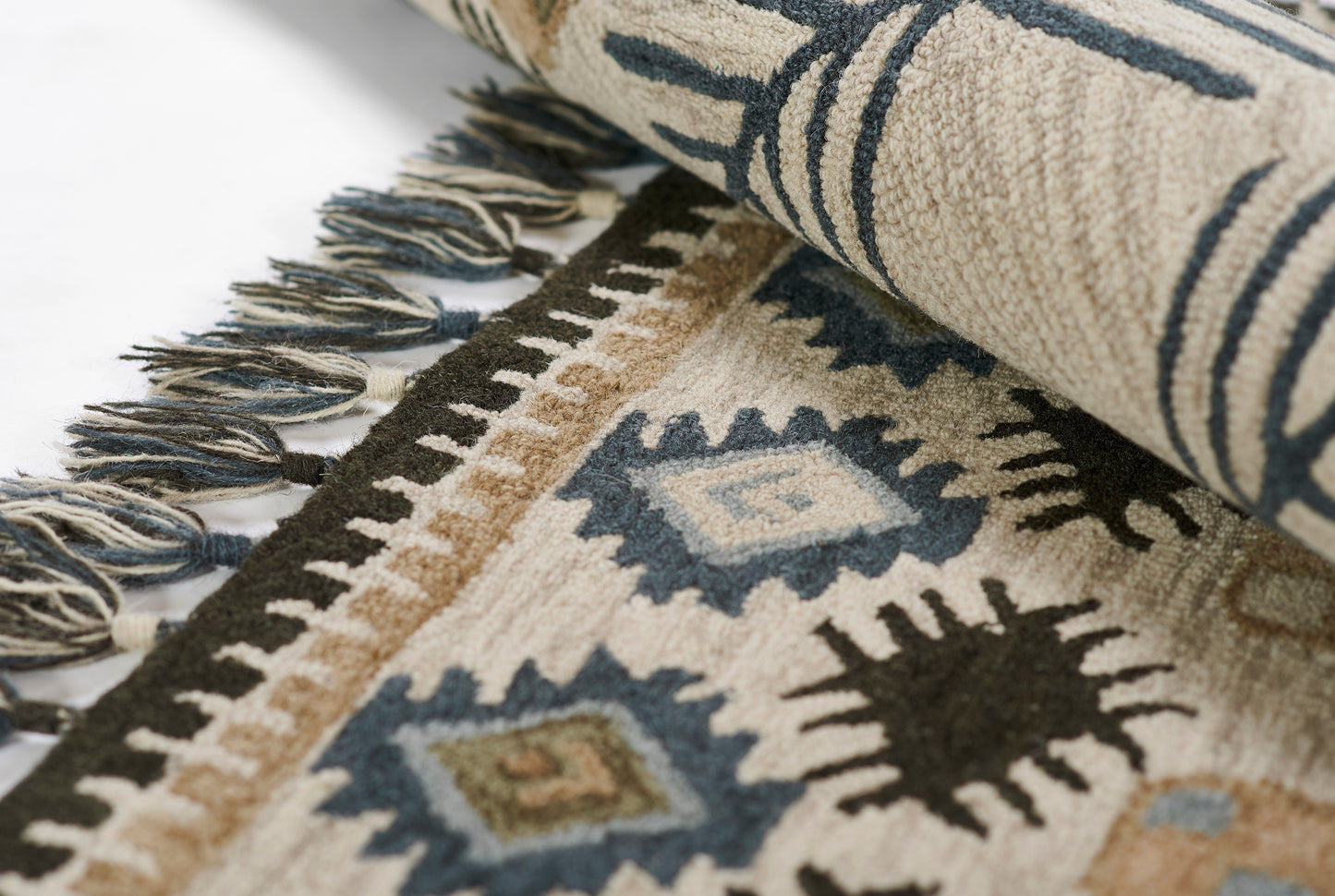 Close-up of beige and navy geometric rug with fringe, featuring diamond motifs and a rolled edge.