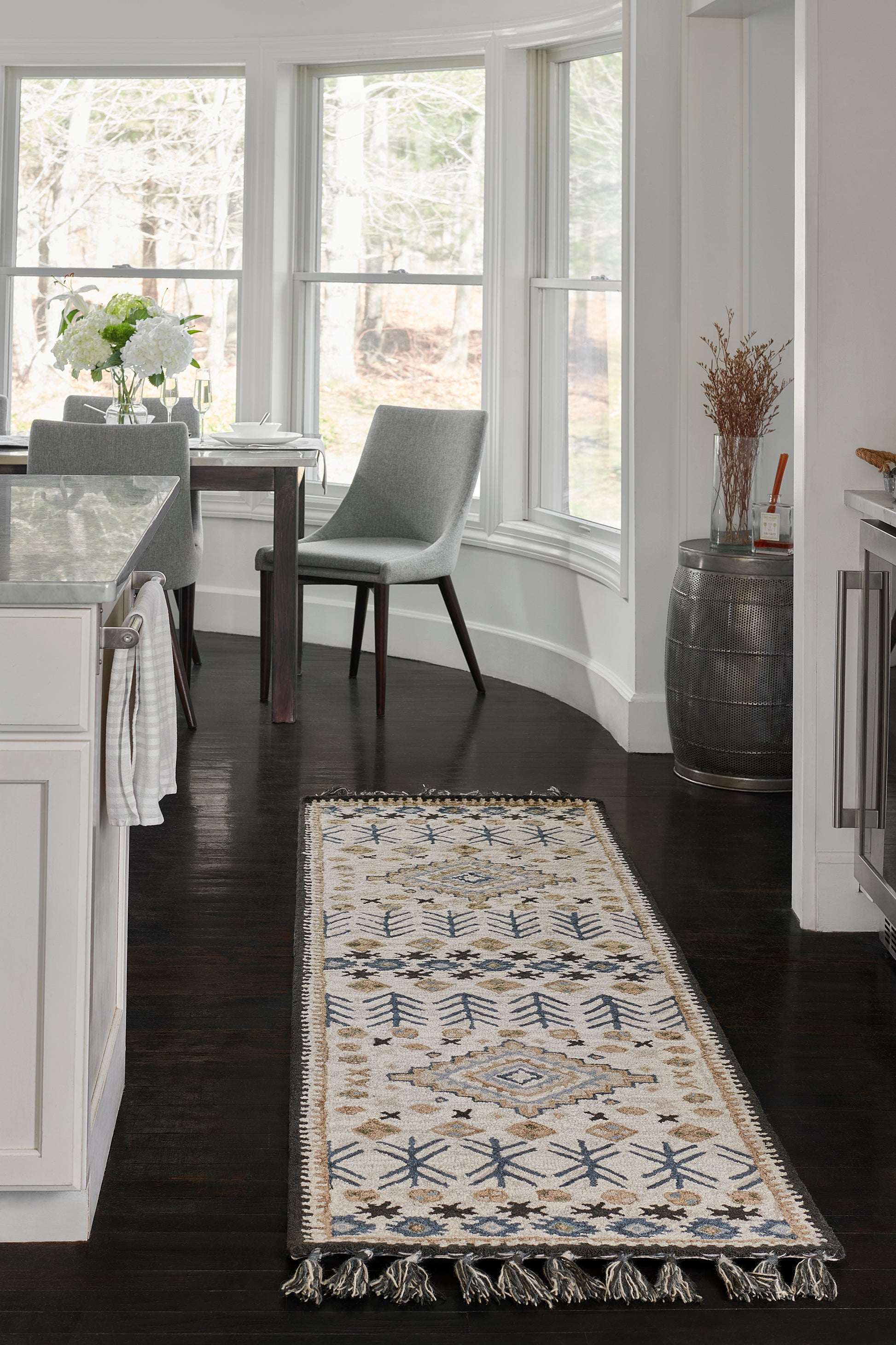 Ivory kilim-style runner rug with blue geometric motifs and fringed ends on a dark hardwood kitchen floor.