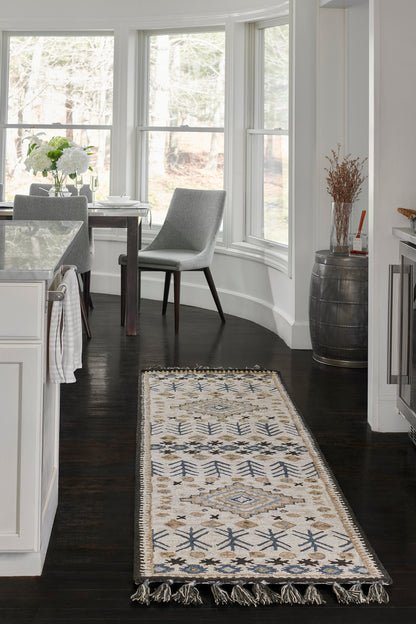 Geometric ivory-blue-beige runner rug with fringe on dark wood floor beside bay windows in a bright kitchen, with grey chairs.