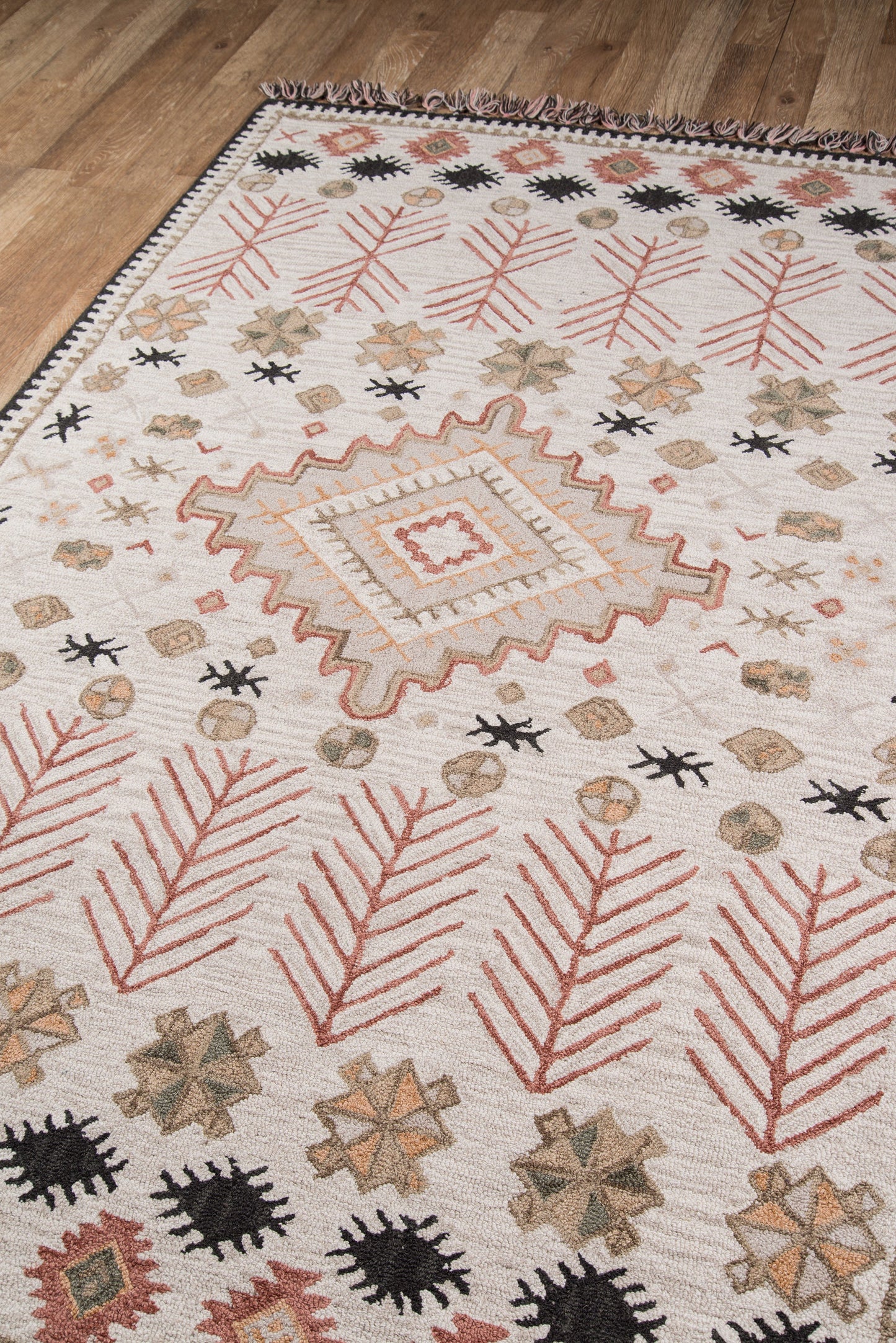 Cream rug with red branch motifs, black sunbursts, star shapes, and a stepped central square medallion on a wood floor.