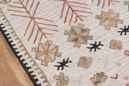 Cream geometric rug with tan, sage and black motifs, red twig patterns, black-and-white bordered fringe on wood floor.