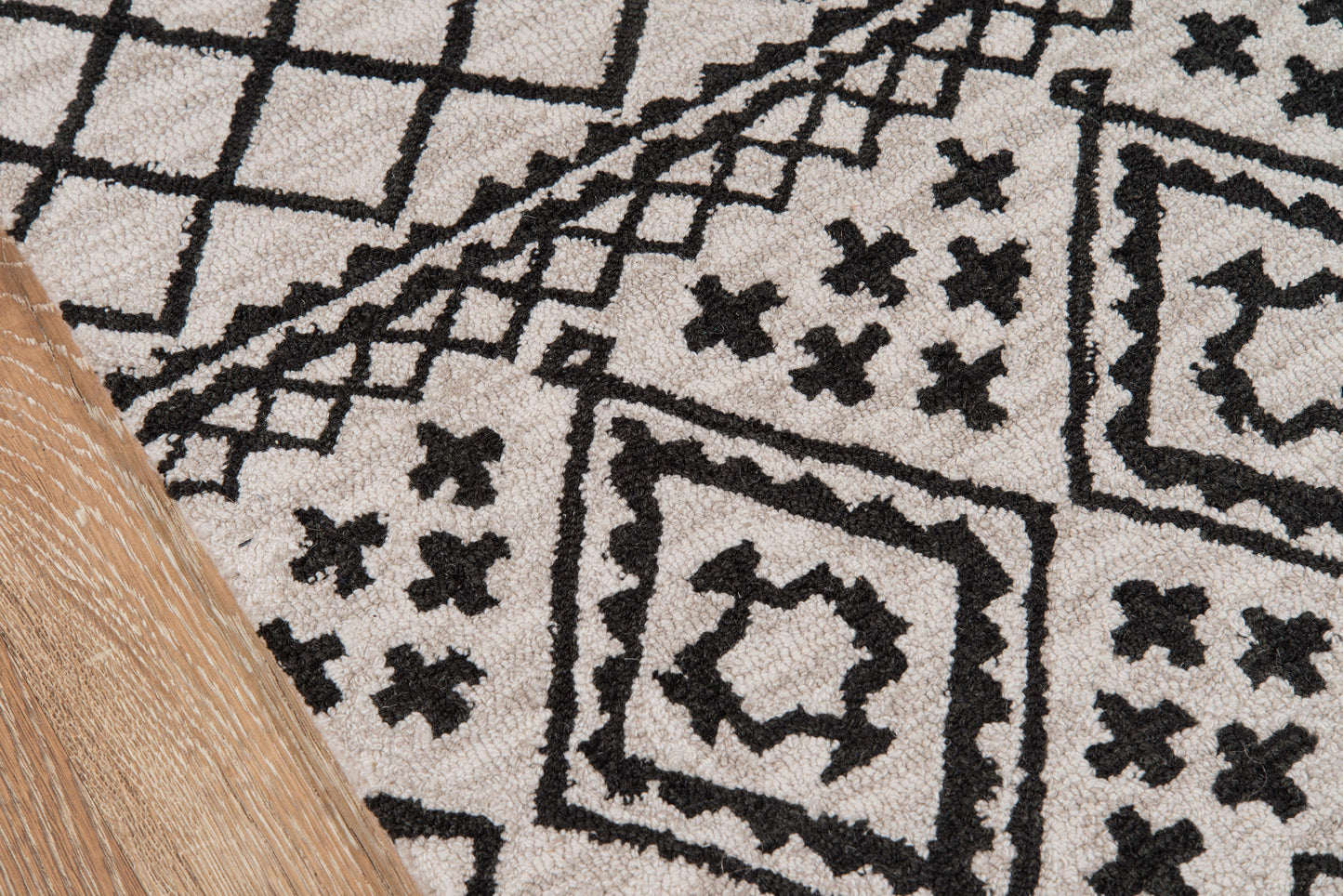 Gray-beige geometric area rug with black diamond and cross motifs, on wooden floor.