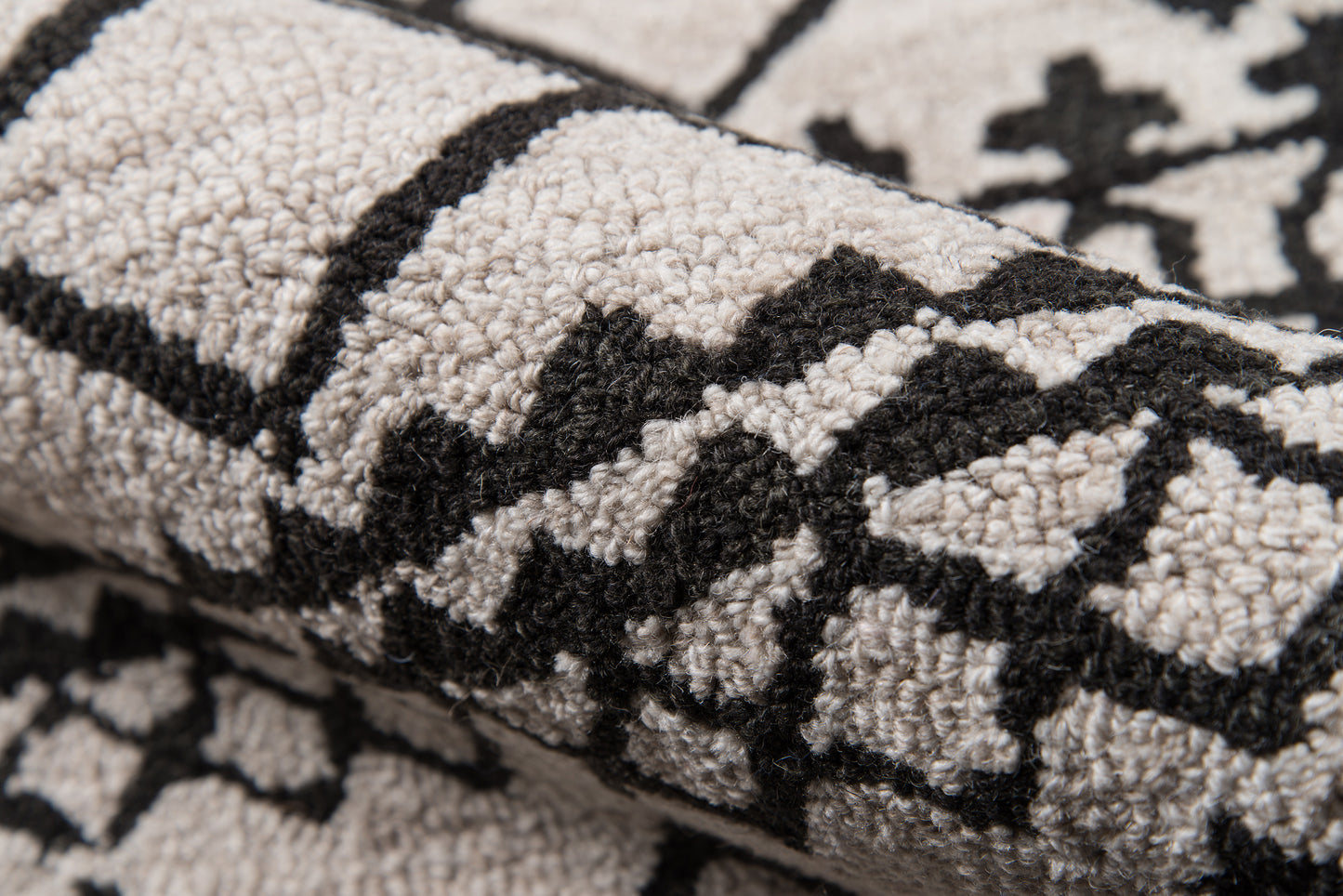 Close-up of a gray rug with a bold black geometric motif; loop-pile texture.