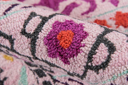 Pink tufted rug with purple flower motif and orange center, dark gray outlines, plush textured pile.