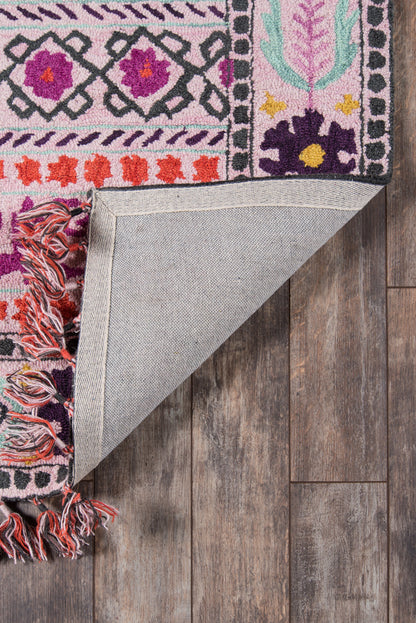 Vibrant pink patterned area rug with purple, orange and teal motifs; folded corner reveals light gray underside and fringe on wood floor.