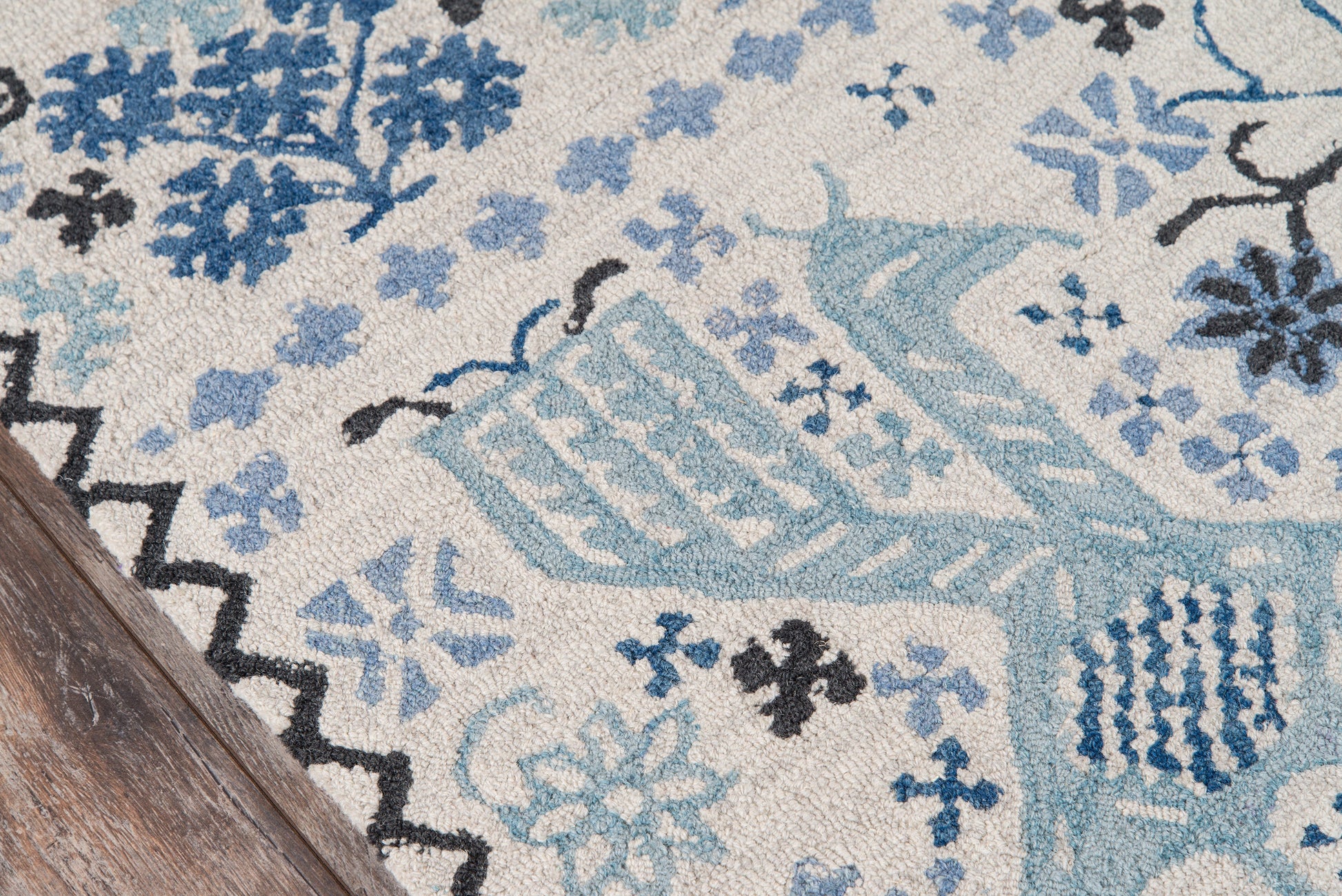 Blue & cream patterned area rug with floral motifs, teal accents, and zigzag border on a wooden floor.