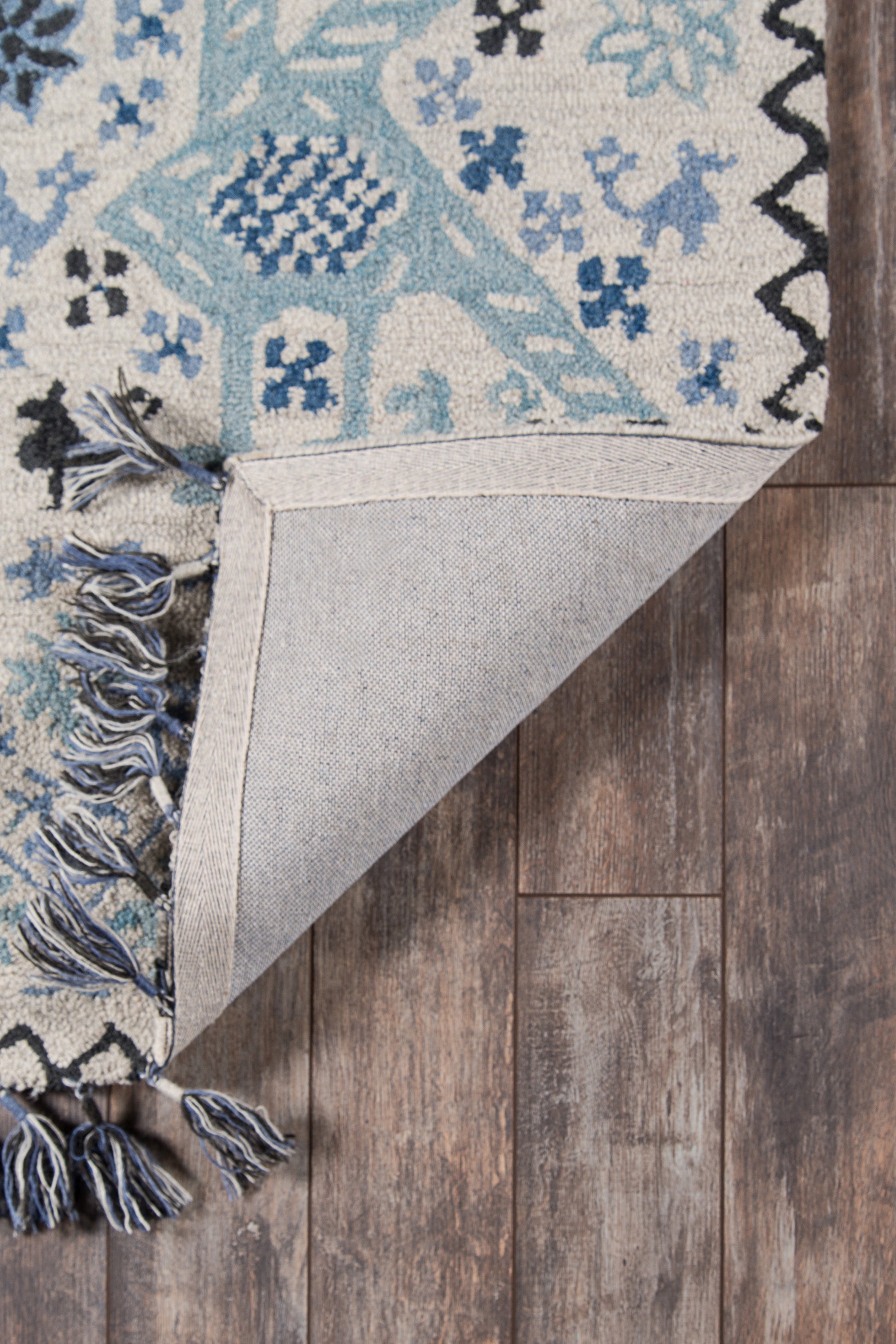 Blue and ivory boho rug with teal accents and fringe, folded corner reveals backing on a wooden floor.