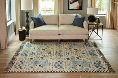 Beige loveseat on a blue-and-cream patterned fringe rug; navy cushions, wood floor, modern living room.