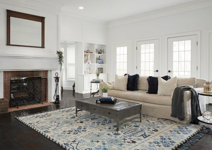 Cozy living room: beige sofa, navy pillows, blue patterned rug, dark metal coffee table, white walls, brick fireplace.