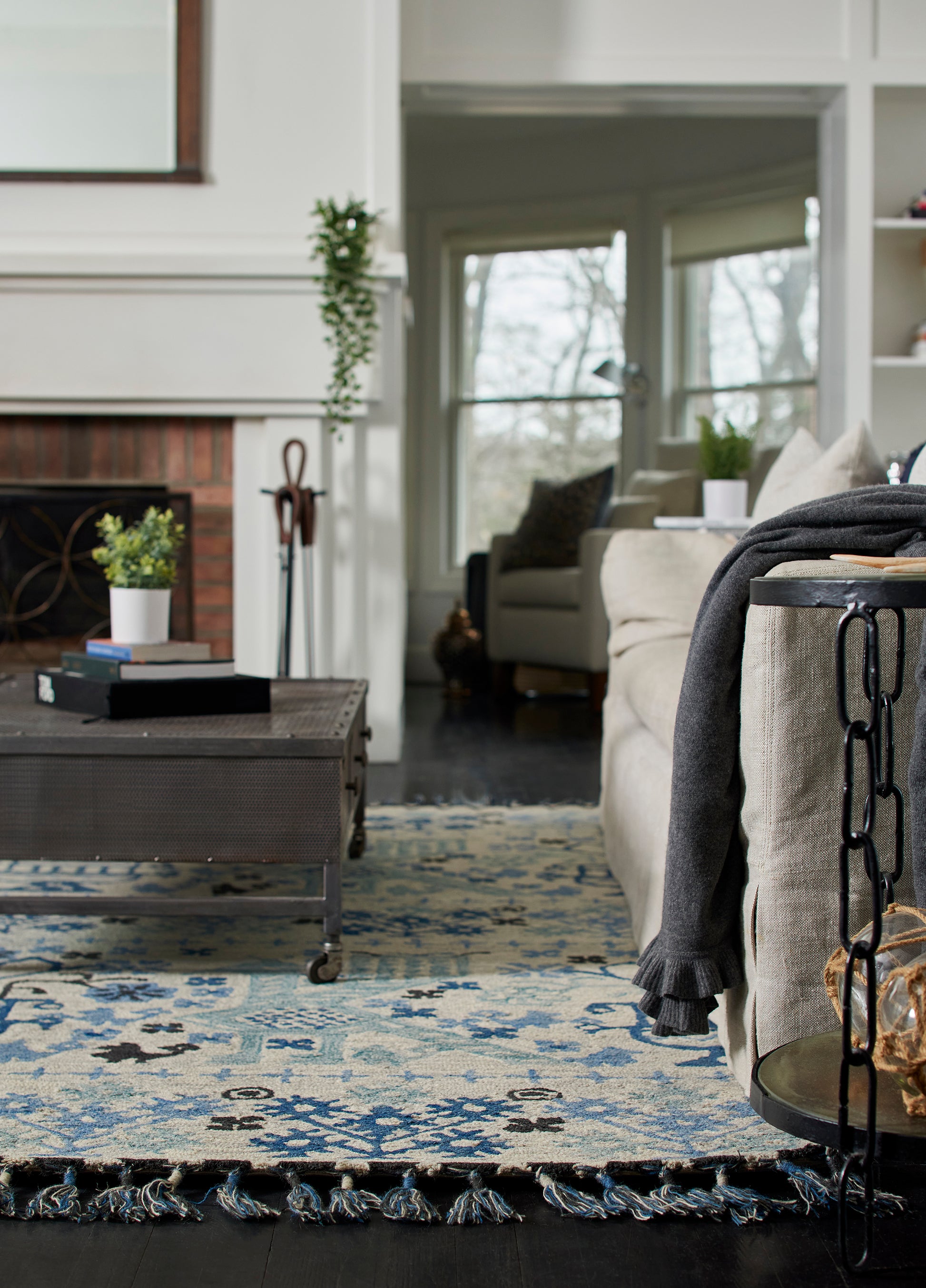 Cozy living room with blue and cream rug, beige sofa, dark gray throw, and a metal wheeled coffee table near the fireplace.