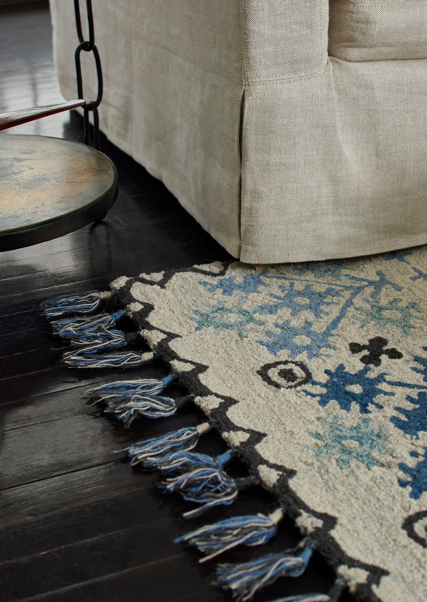 Blue and cream patterned rug with fringe on a dark wood floor; nearby beige sofa and a round swing chair frame.