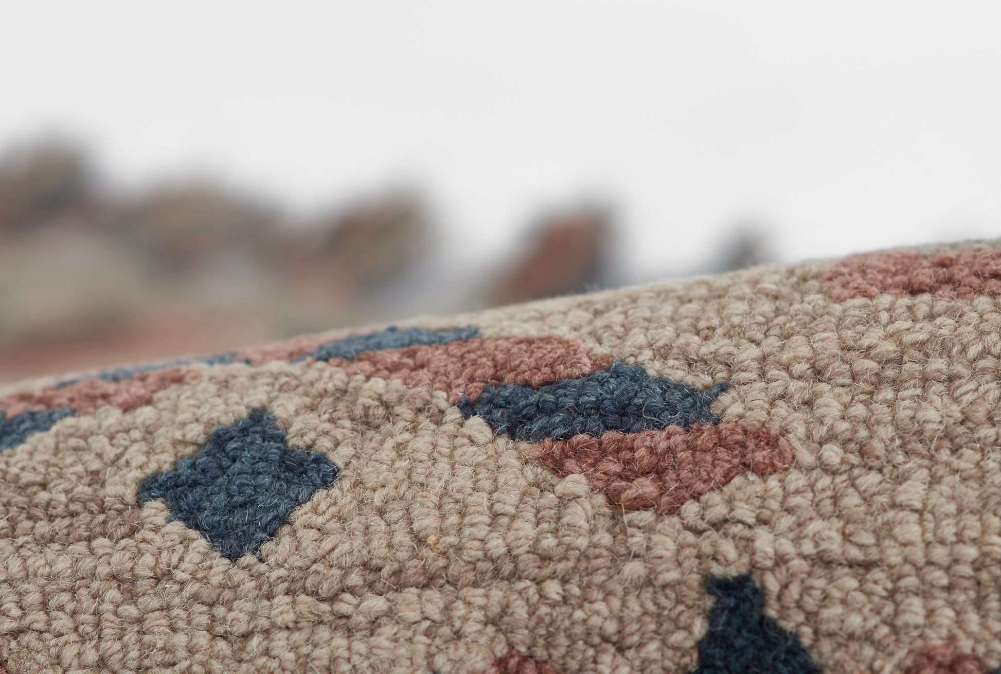 Close-up of beige tufted rug with dark blue and rust geometric shapes, dense loop pile.