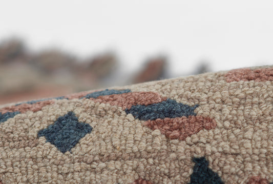 Close-up of beige tufted rug with dark blue and rust geometric shapes, dense loop pile.