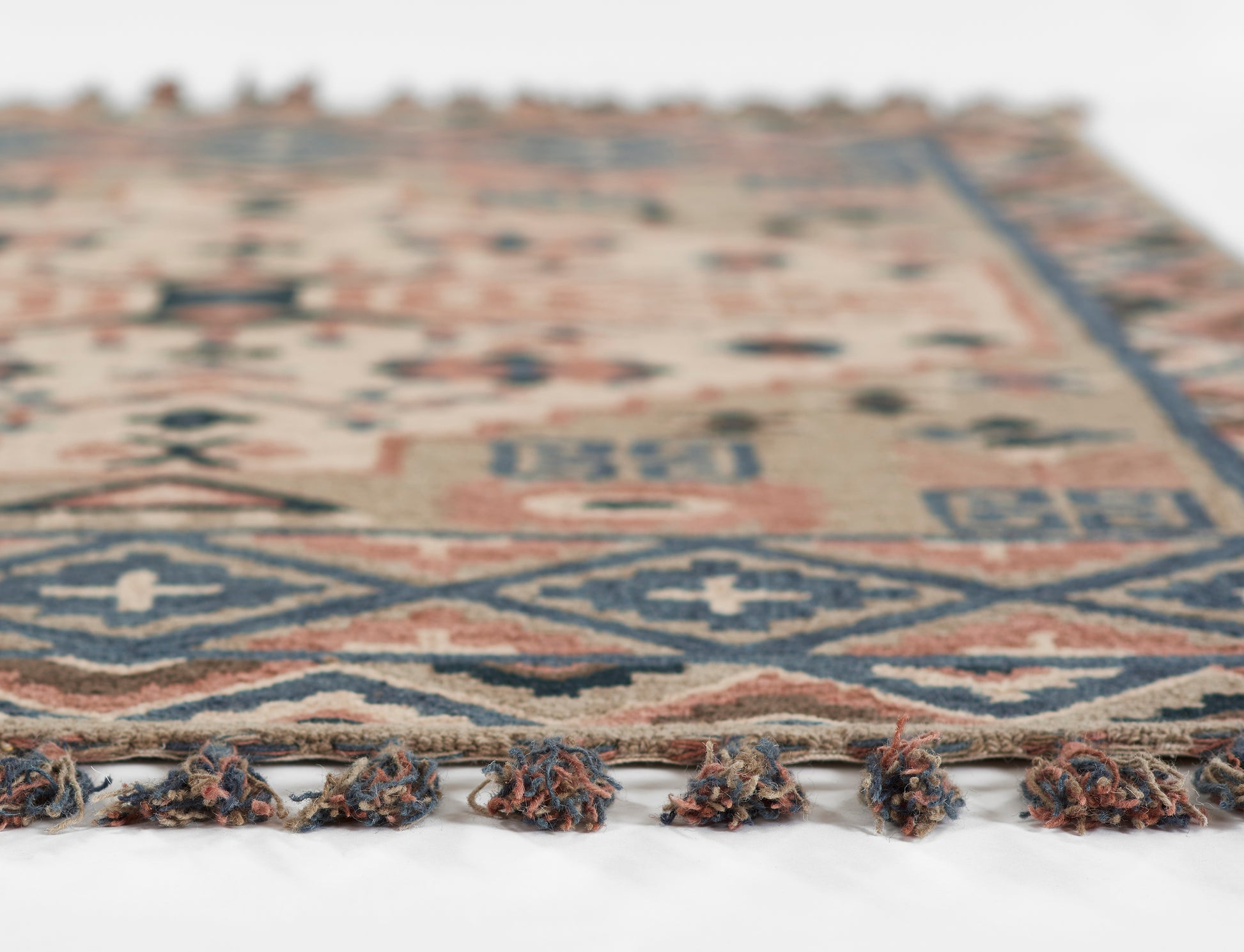 Geometric area rug in blue, beige and rust with fringe tassels along the edge, soft woven texture.