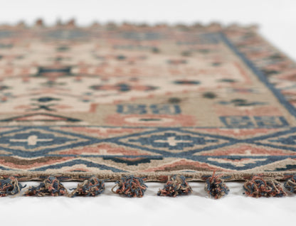 Geometric area rug in blue, beige and rust with fringe tassels along the edge, soft woven texture.