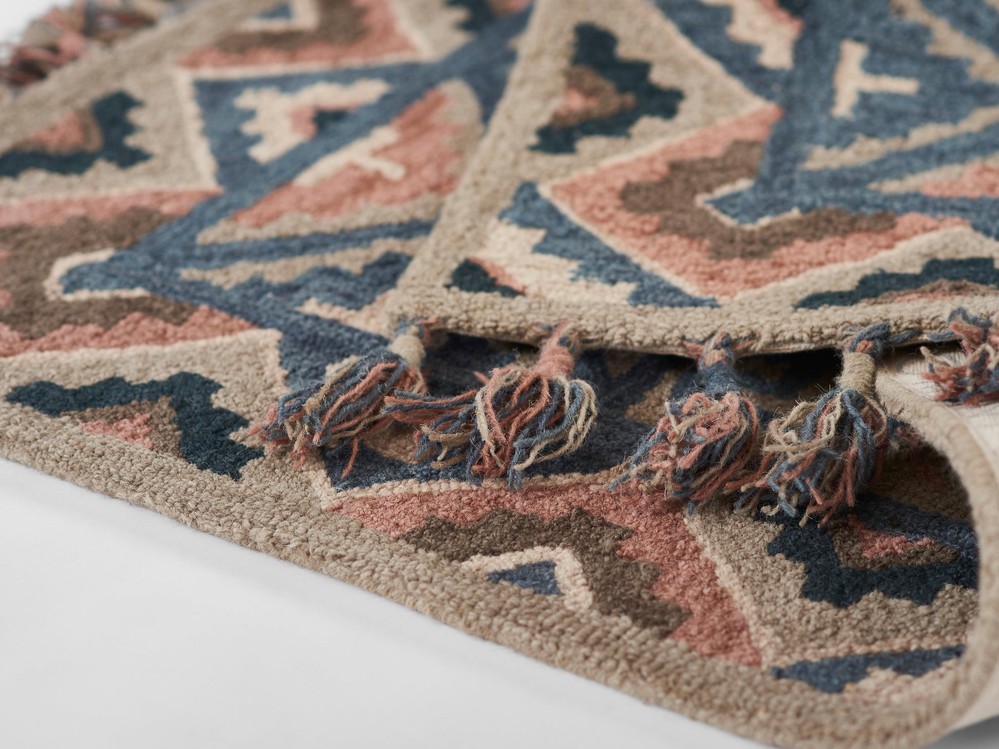 Aztec-inspired geometric rug in beige, navy, pink and brown with fringe tassels.