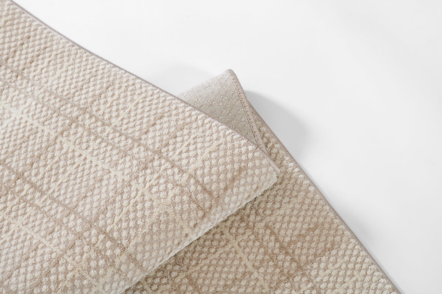 Beige textured rug with small raised dot pattern; folded corner reveals soft underside.