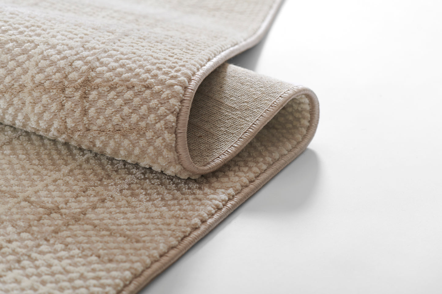 Beige textured loop-pile rug with bound edges, rolled to reveal its underside; soft, neutral rug.