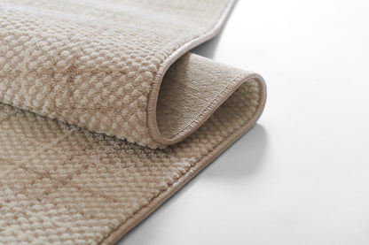 Beige rectangular plush rug with rolled taupe binding and soft looped pile.
