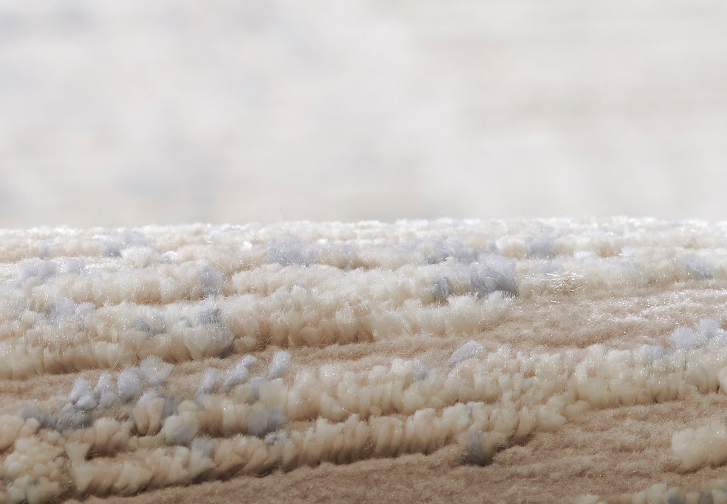 Beige shag rug close-up with thick plush pile in cream & pale blue-gray fibers.