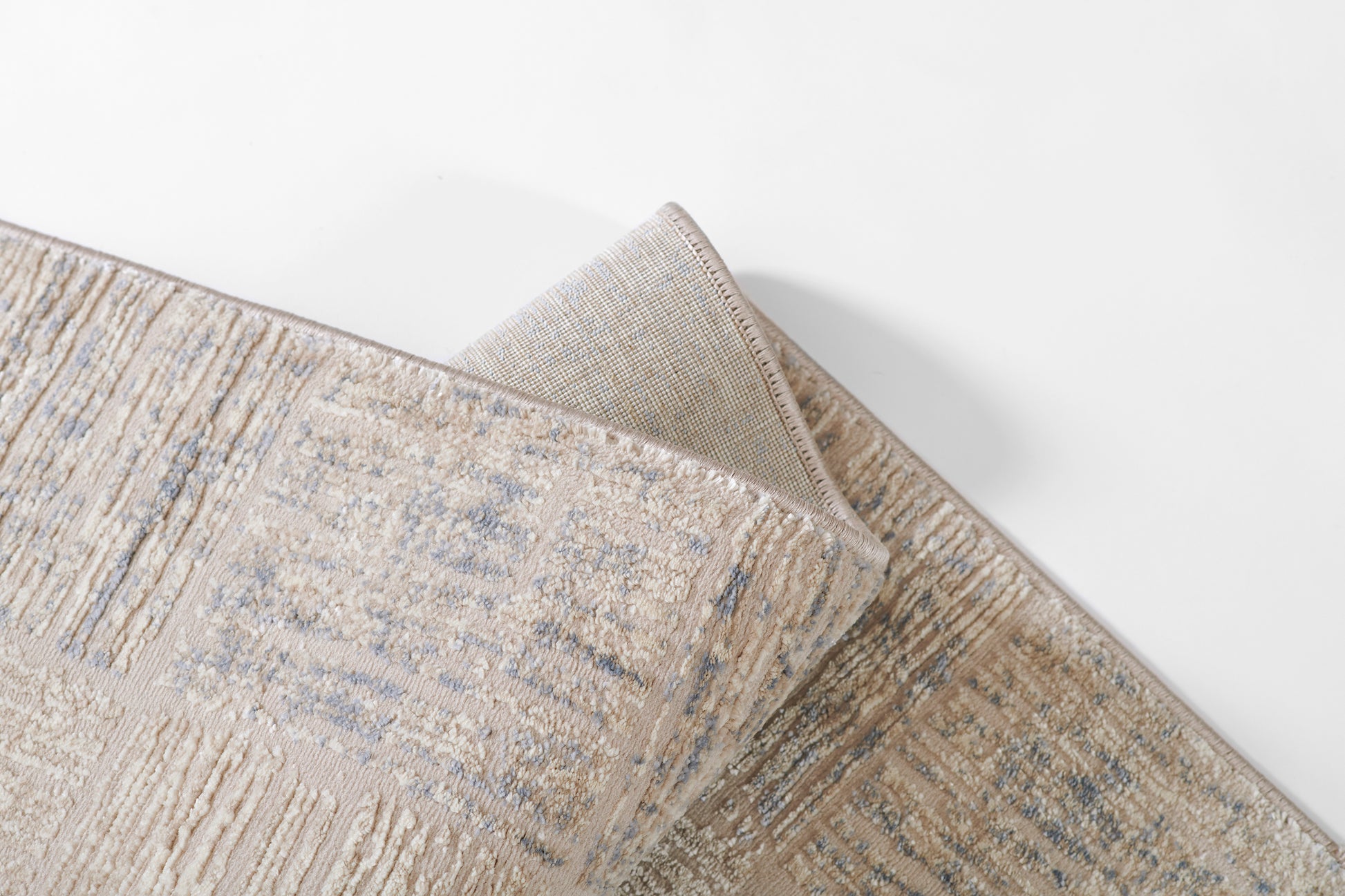 Beige woven rug with subtle blue abstract pattern & textured pile, folded corner.