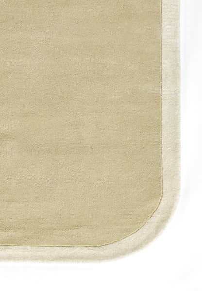 Beige rectangular rug with rounded bottom-right corner and pale border; soft textured surface.