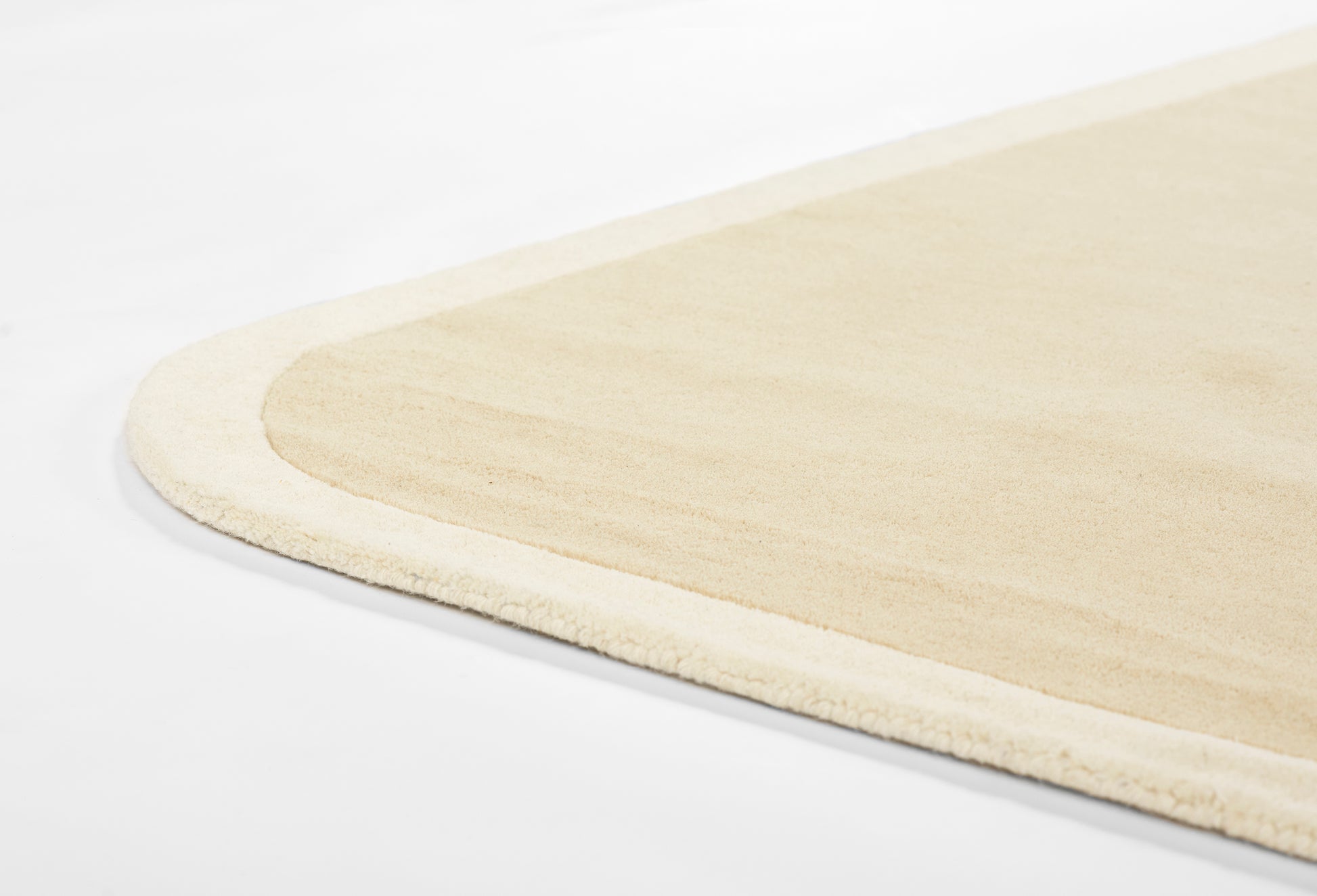 Beige plush rug with soft fringe edge and rounded corner; modern cozy floor decor.