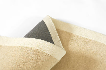 Beige rug with light border and dark gray underside, showing a folded edge and soft textured weave.