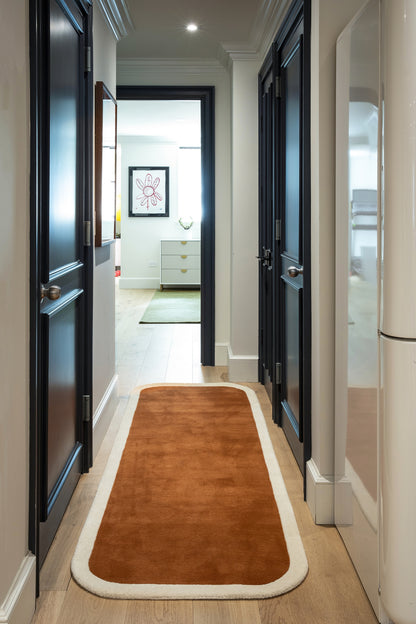 Rust-orange runner rug with white border in a narrow hallway with dark navy doors and light walls.