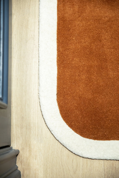 Close-up of burnt orange plush rug with white border on light wood floor, featuring a rounded corner.