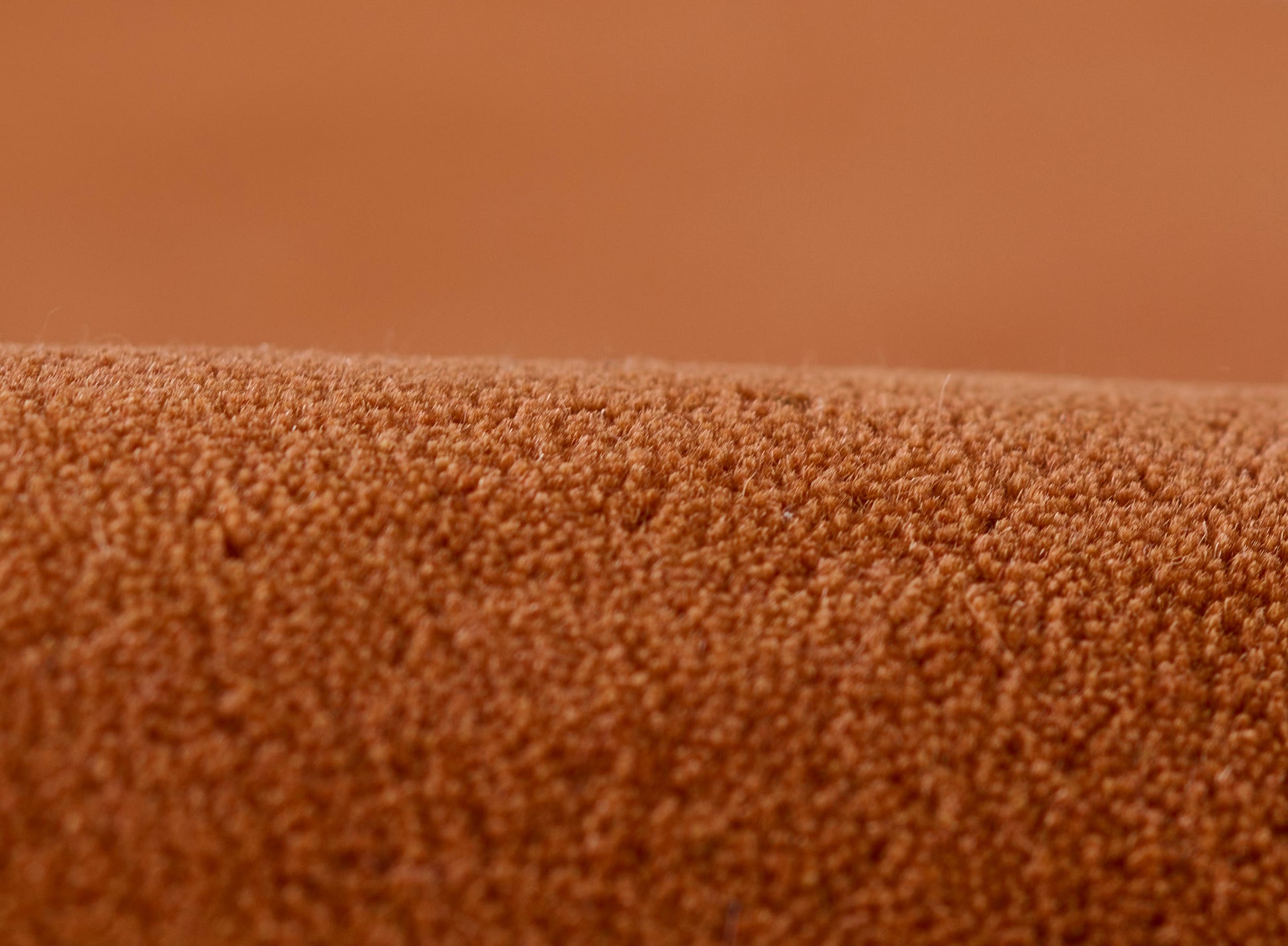 Burnt-orange carpet close-up with dense micro-tufted loop-pile texture.