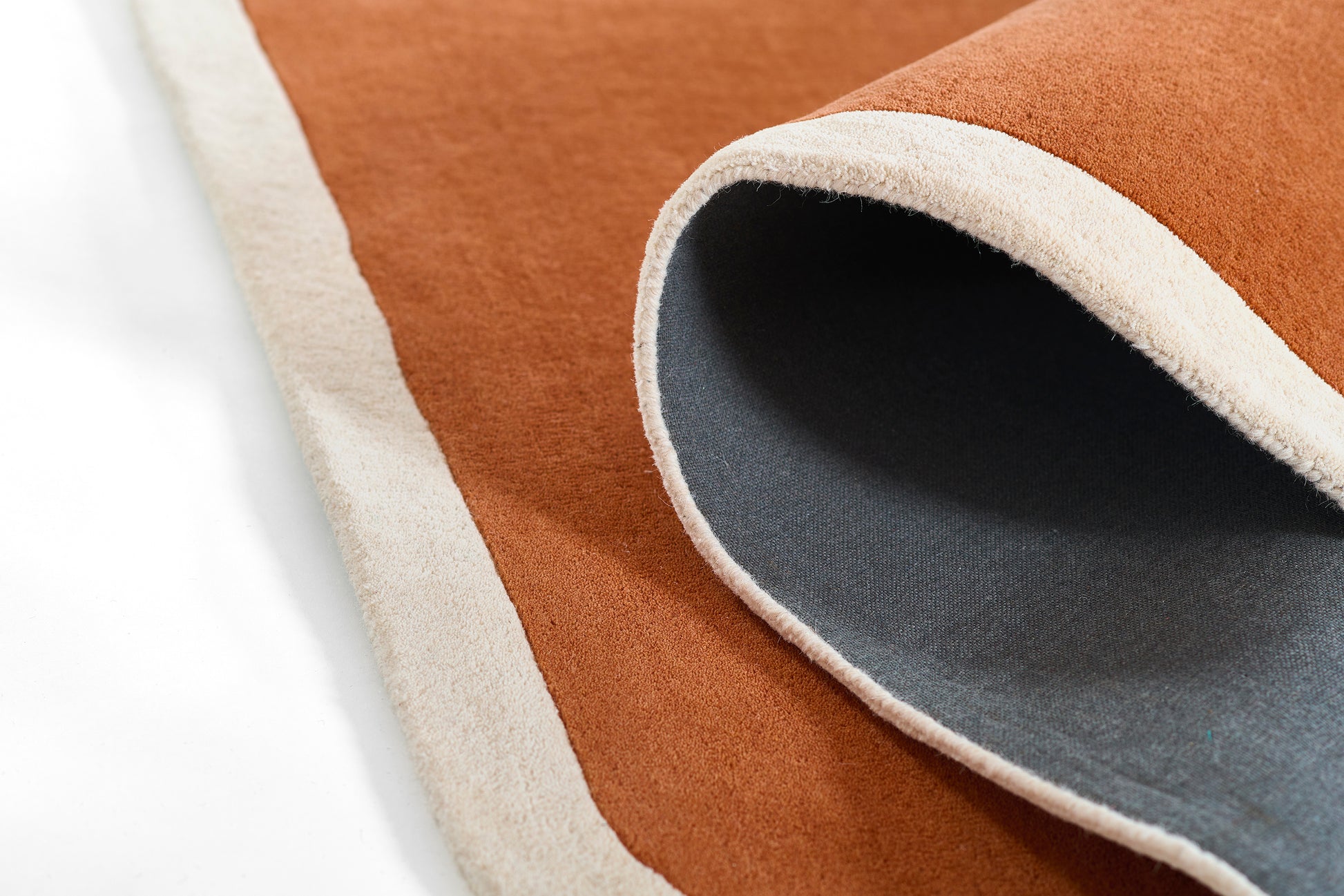Terracotta orange rug with cream border, rolled edge reveals gray underside.