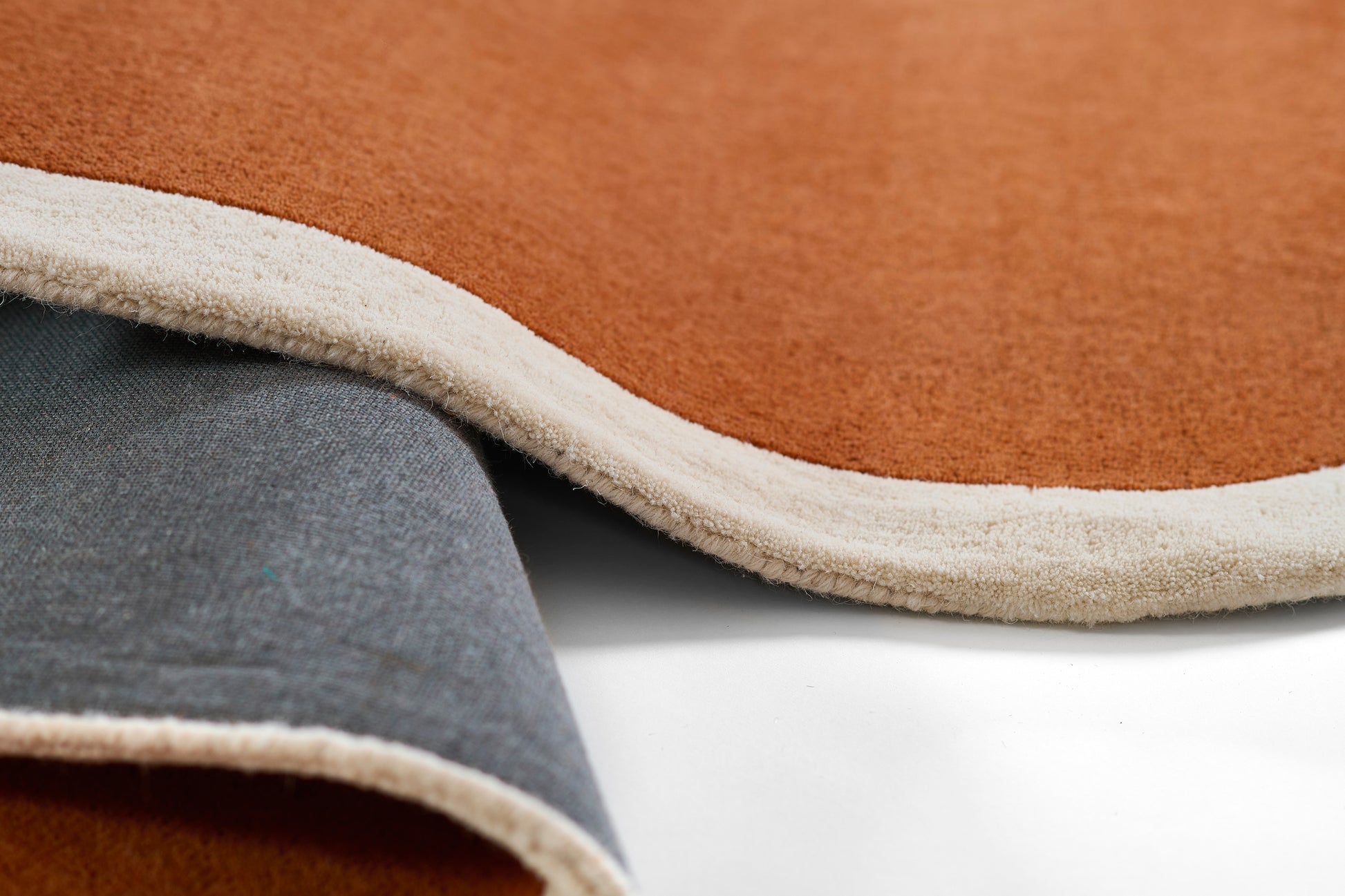 Rust brown plush rug with cream edge binding and gray underside, soft floor mat.