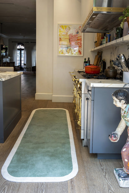 Teal-green rectangular kitchen runner rug with a white border, long and narrow on wood flooring in a modern kitchen.