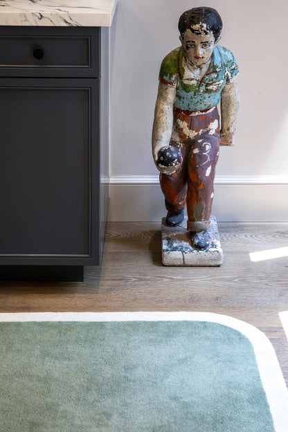 Green-toned area rug with a subtle pattern, placed on the floor.