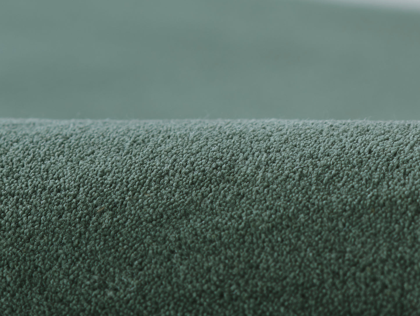 Green loop-pile rug fabric, close-up of dense textured surface with rolled edge.
