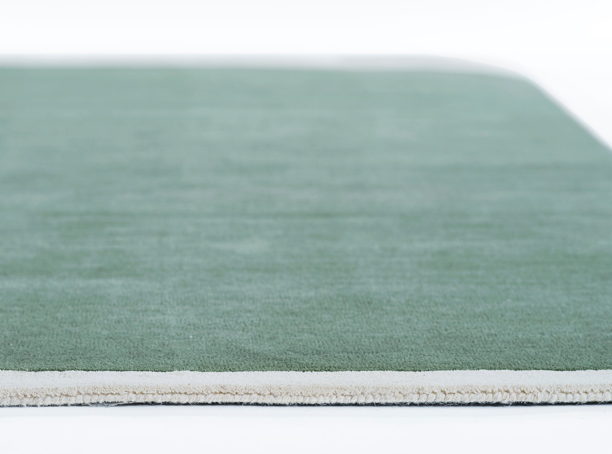 Sage green rug with light beige binding along the edge; low-pile texture for a modern, minimalist living space.