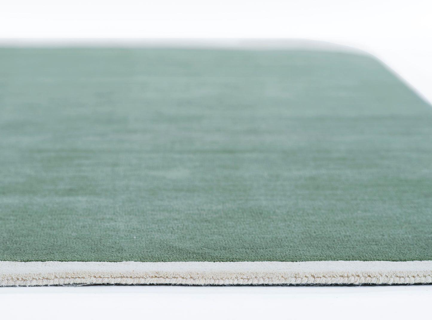 Green flat-weave rug with cream fringe along edge; rectangular, modern minimalist style.