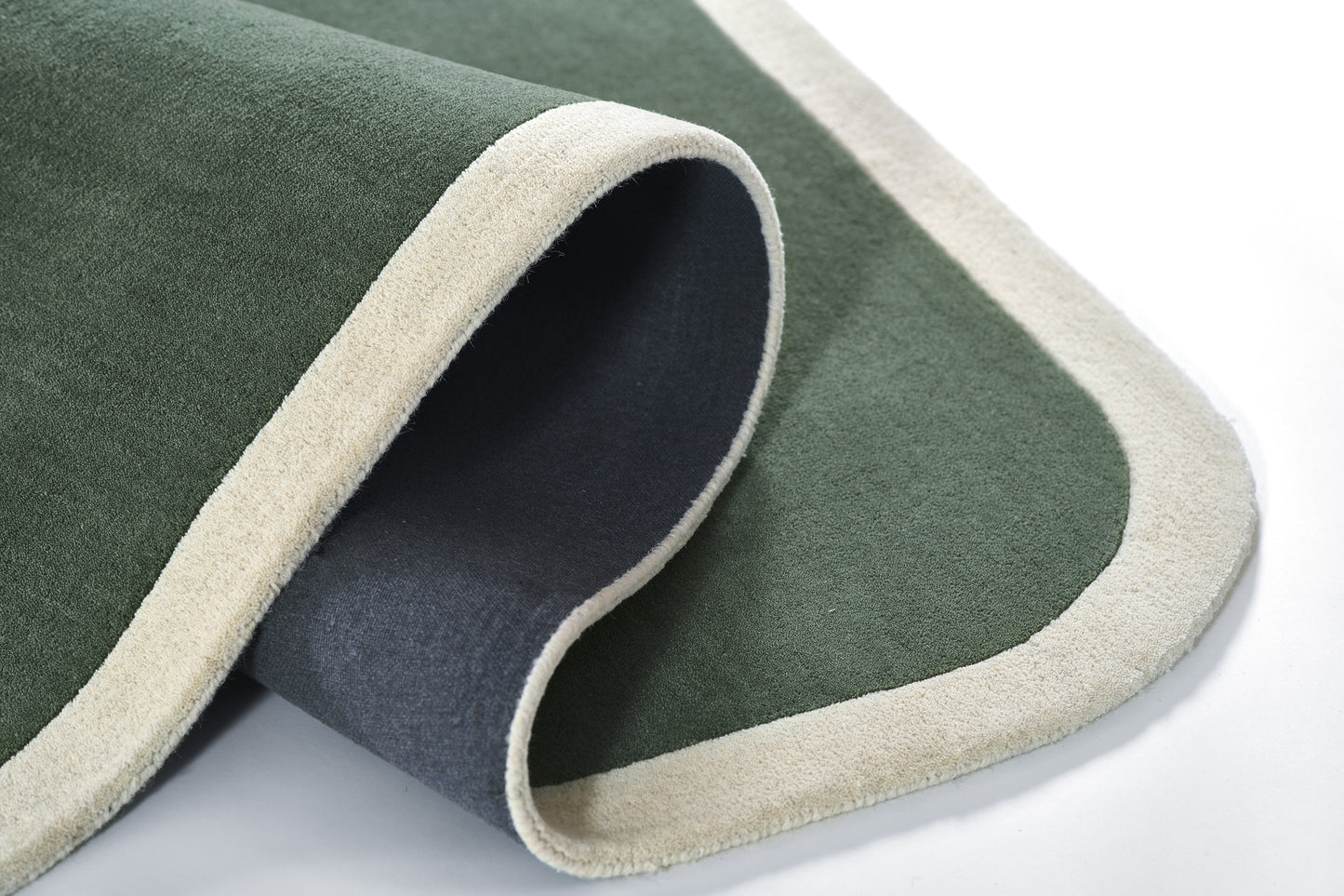 Green rug with beige outer border, rolled to show gray underside; soft, plush floor covering.