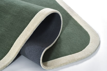 Green rug with cream edging, soft pile, rolled corner and gray underside; modern indoor decor.