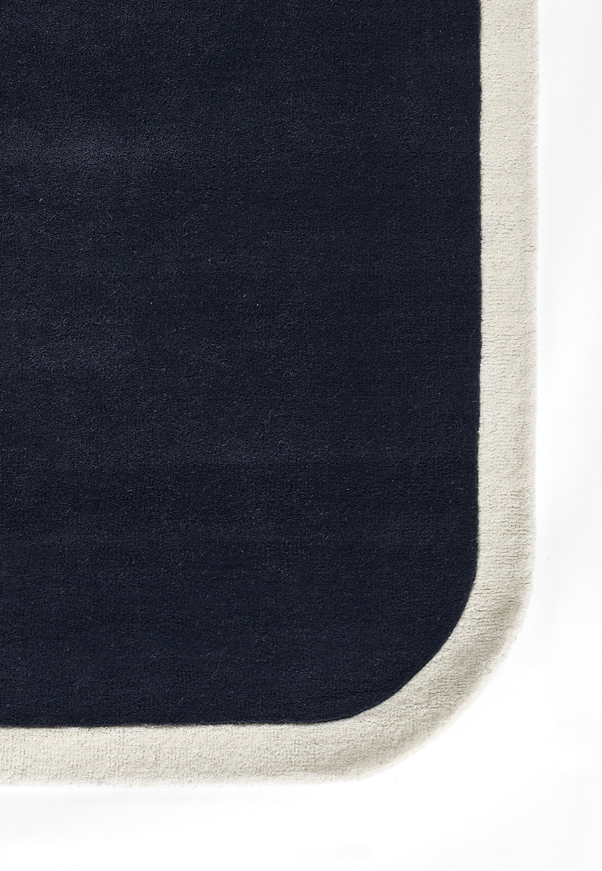 Dark navy rug with cream fringe border and rounded corner; plush, modern floor mat.