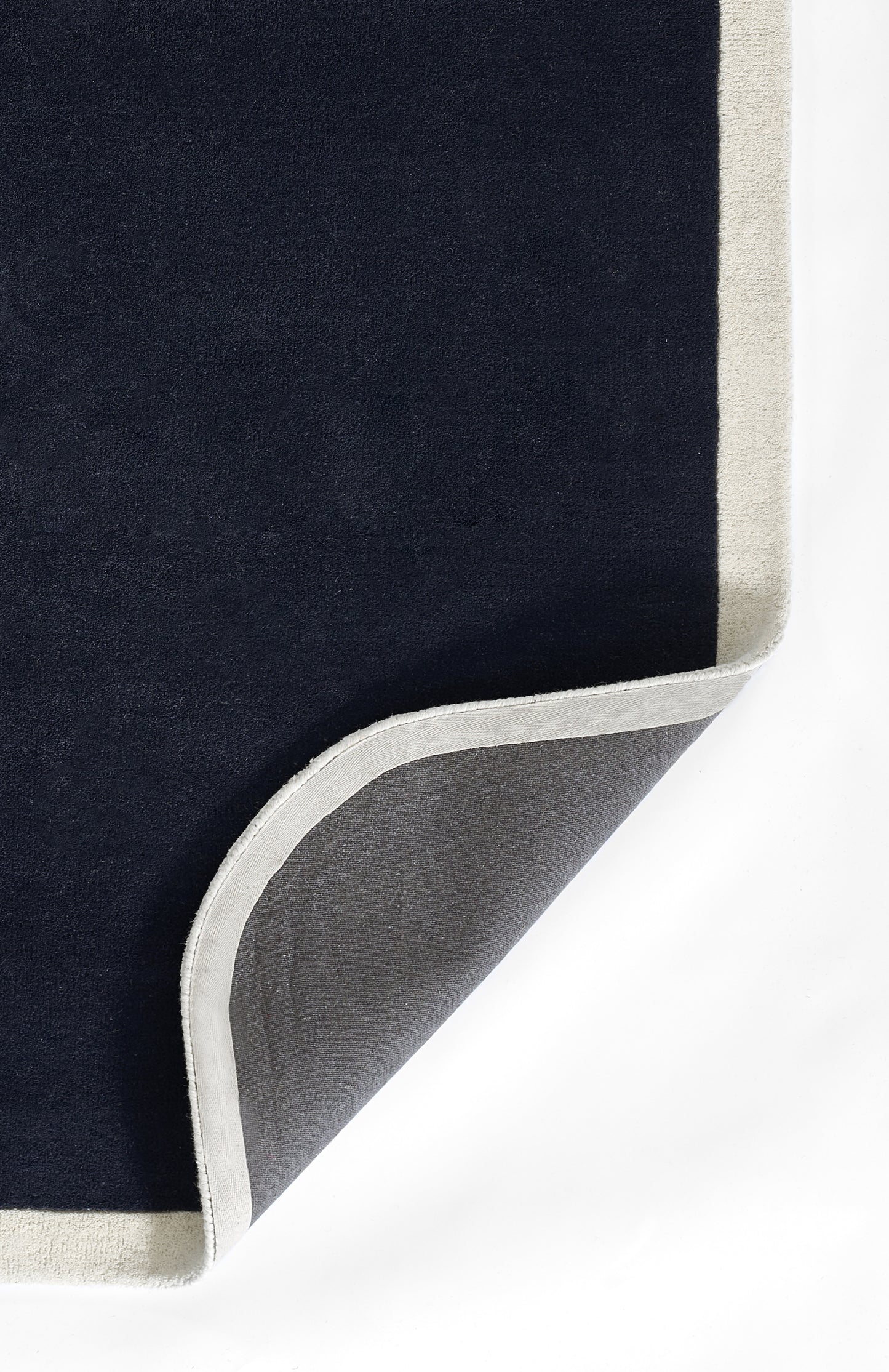 Navy rug with cream border and grey underside, folded corner; plush, soft textile.