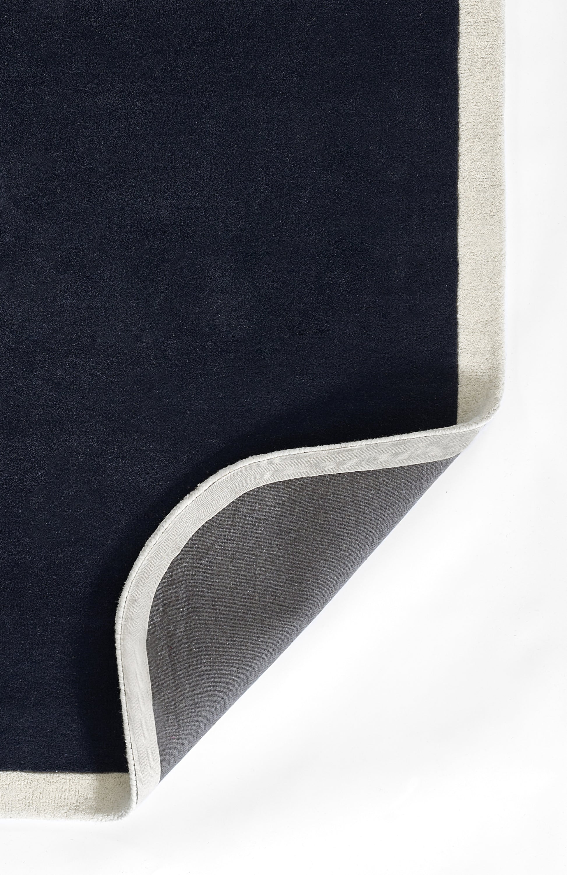 Navy rug with cream border and grey underside, folded corner; plush, soft textile.