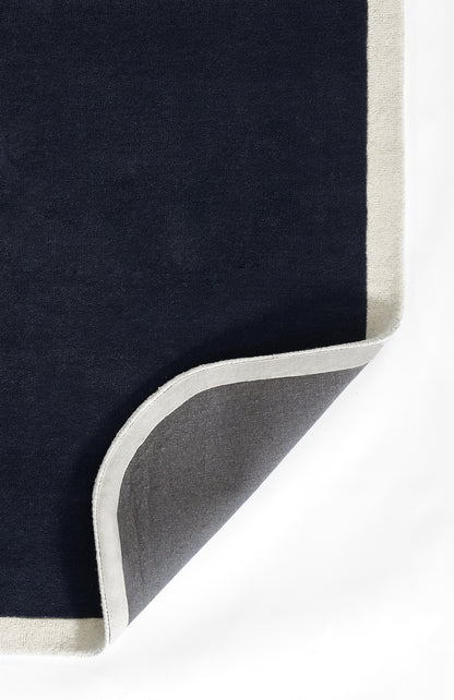 Navy rectangular rug with pale beige border; rounded folded corner shows gray backing.