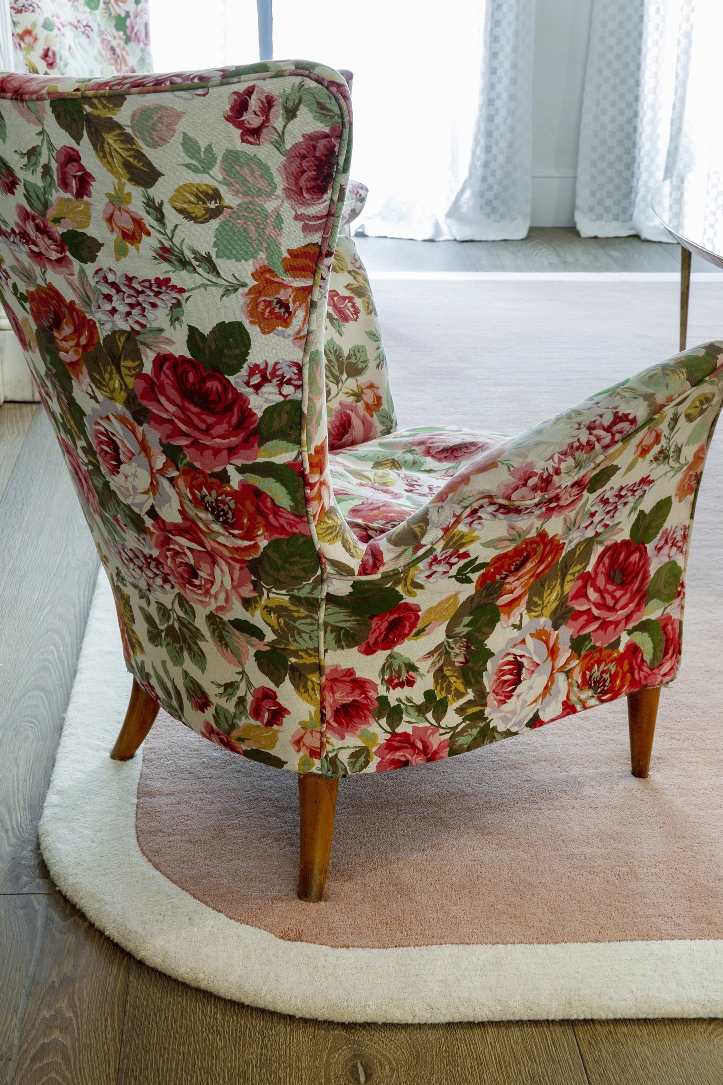 Floral upholstered armchair with pink roses and green leaves on cream fabric; curved back and wooden legs.