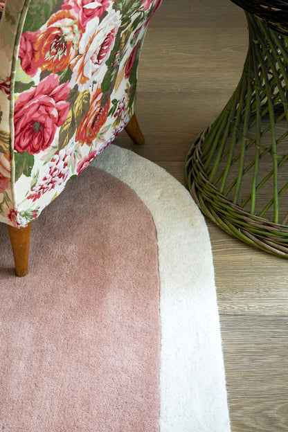 Floral pink & red upholstered chair with wooden legs beside a pink circular rug on a wood floor and a green wicker piece.